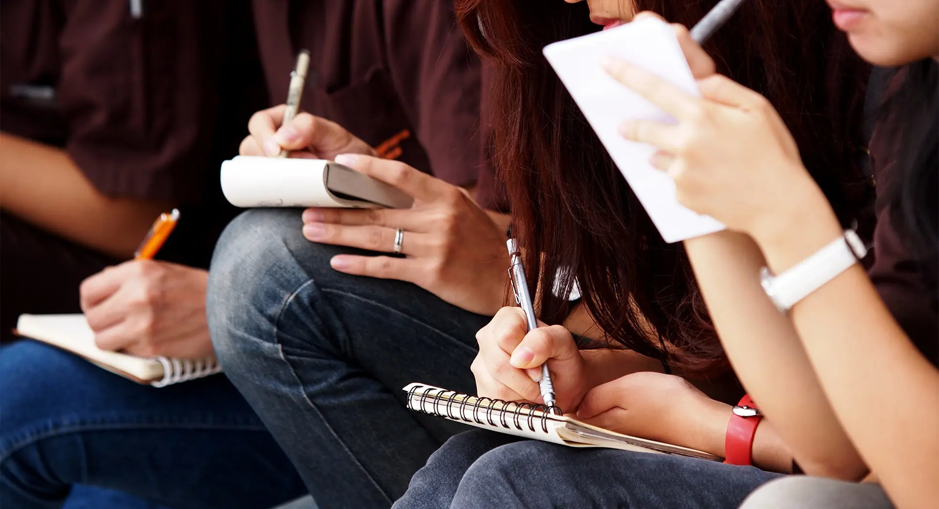 A close-up of a group of students writing in notepads