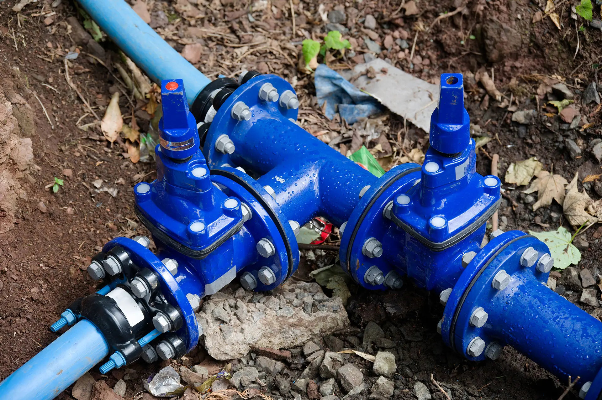 A close-up of a blue water main on the ground connected to blue pipes